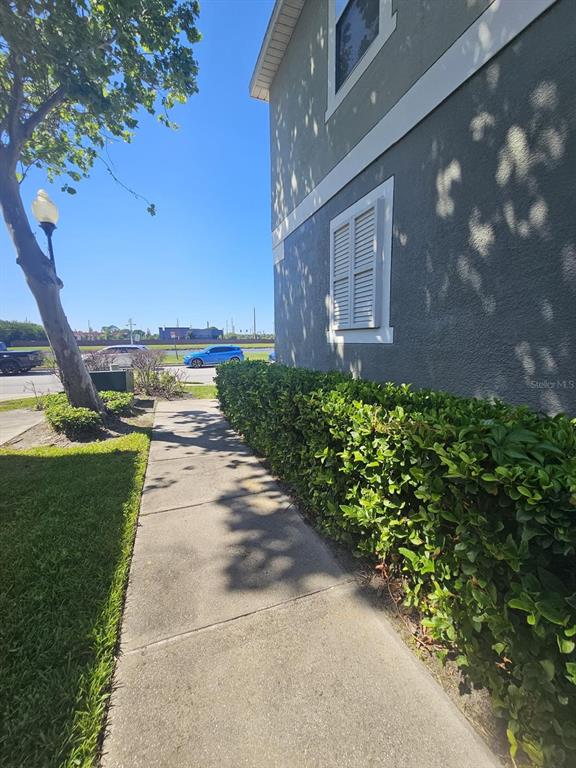 A concrete sidewalk runs alongside a building exterior with a hedge and a tree — 1917 ESTANCIA CIRCLE, KISSIMMEE, FL