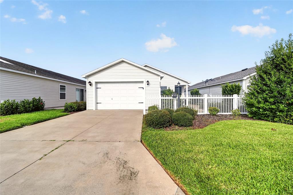 A white single-story house features a concrete driveway, a garage, and a white picket fence — 5844 MARSH COURT, THE VILLAGES, FL