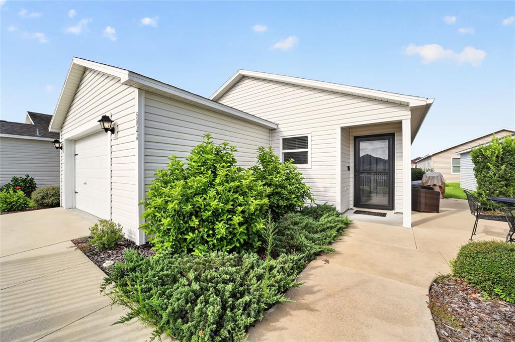 A light-colored vinyl-sided house features a garage, a front entryway, and landscaped shrubbery — 5844 MARSH COURT, THE VILLAGES, FL