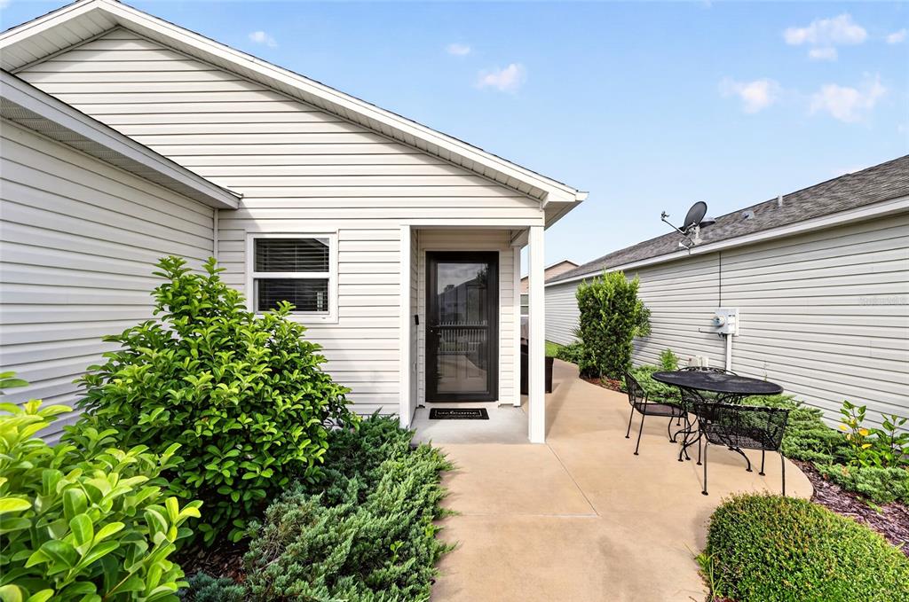 A light-colored vinyl-sided house exterior features a front door, a concrete patio, and landscaping — 5844 MARSH COURT, THE VILLAGES, FL