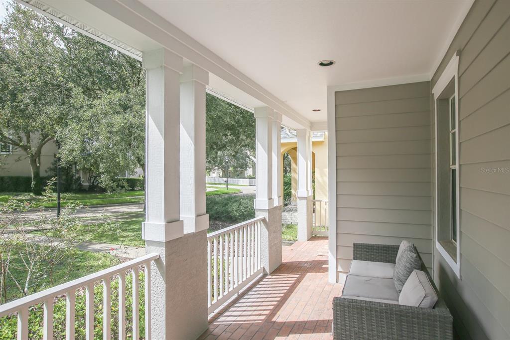 A covered porch features white railings, square columns, brick flooring, and a gray wicker sofa — 16244 BRIDGEWALK DRIVE, LITHIA, FL