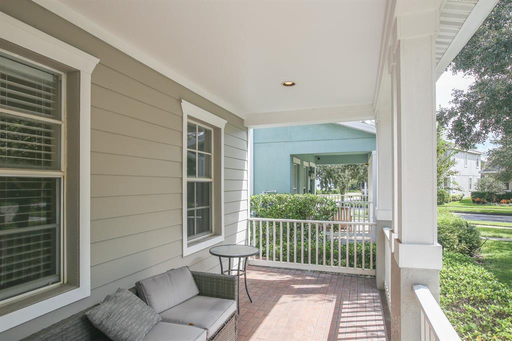 A covered porch features a brick floor, light-colored siding, and a small outdoor seating area — 16244 BRIDGEWALK DRIVE, LITHIA, FL