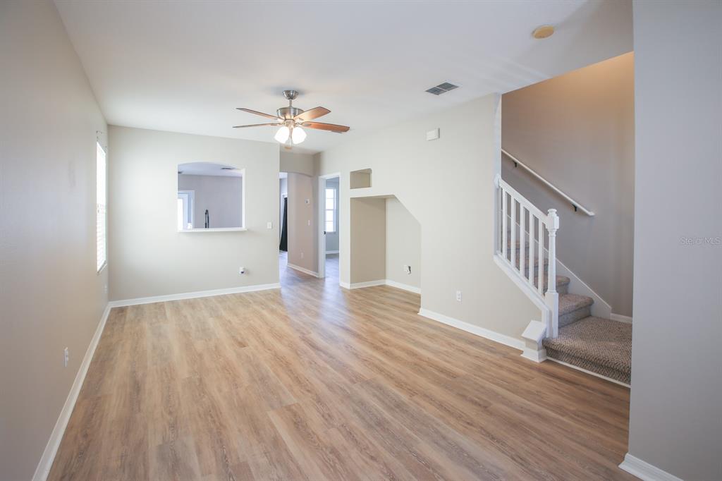 An empty living room features light wood-look flooring, a ceiling fan, and a carpeted staircase — 16244 BRIDGEWALK DRIVE, LITHIA, FL