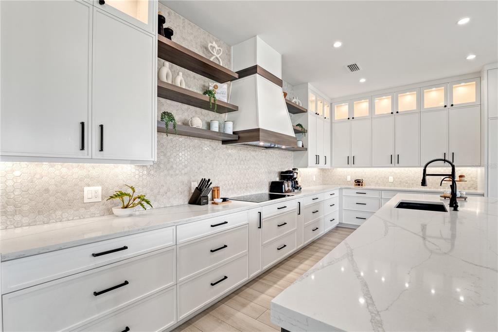 A modern white kitchen features marble countertops, open shelving, a range hood, and dark hardware — 171 MCKINLEY DRIVE, SARASOTA, FL