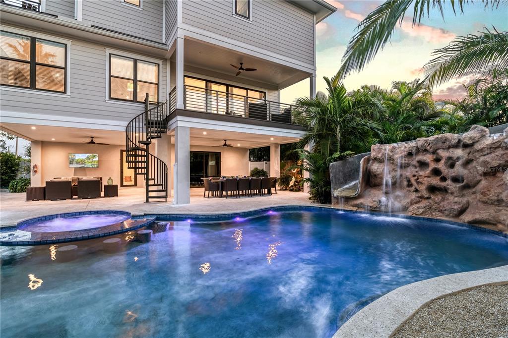 A backyard pool with a rock waterfall and slide sits beneath a two-story house exterior — 171 MCKINLEY DRIVE, SARASOTA, FL
