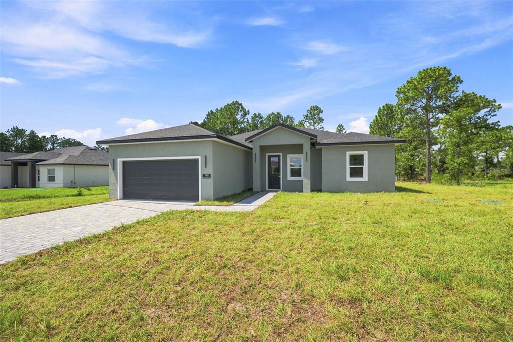 A single-story house with a gray stucco exterior, a two-car garage, and a paved driveway — 748 MARION OAKS MANOR, OCALA, FL