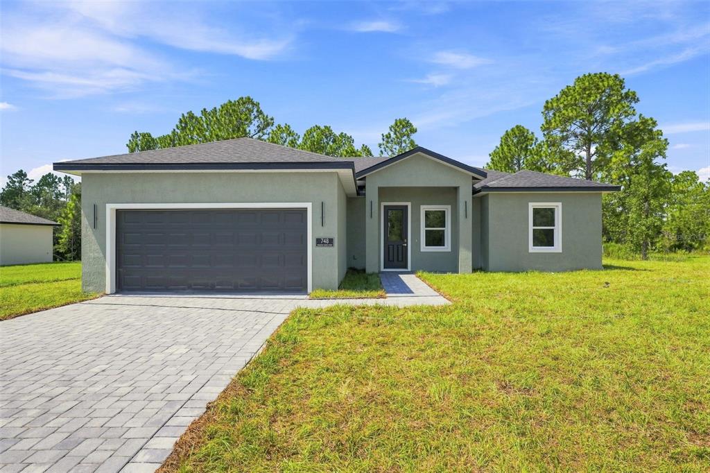 A single-story house with a gray stucco exterior, a two-car garage, and a paved driveway — 748 MARION OAKS MANOR, OCALA, FL