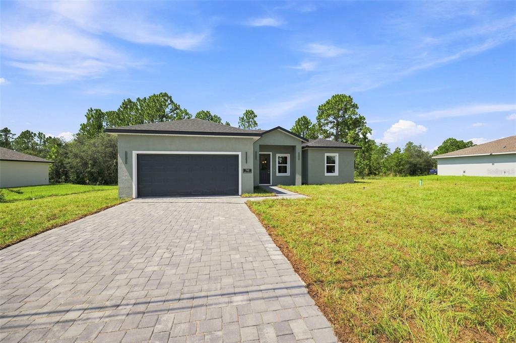 A single-story house with a gray stucco exterior, a paved driveway, and a two-car garage — 748 MARION OAKS MANOR, OCALA, FL