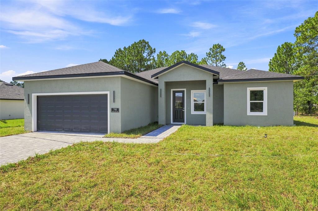 A single-story house with a gray stucco exterior, a two-car garage, and a paved walkway — 748 MARION OAKS MANOR, OCALA, FL