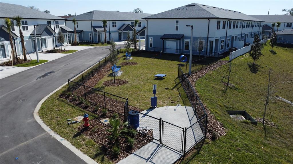 An aerial view shows a fenced-in dog park situated between residential townhome buildings — 1075 E CAROLINE STREET, TAVARES, FL