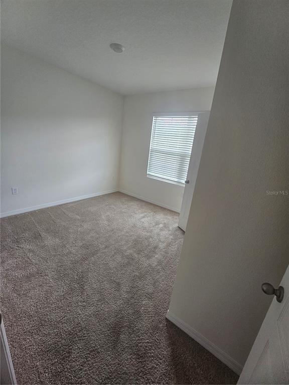 An empty bedroom features beige carpet, white walls, and a window with closed blinds — 1504 FOX SQUIRREL DRIVE, DAVENPORT, FL