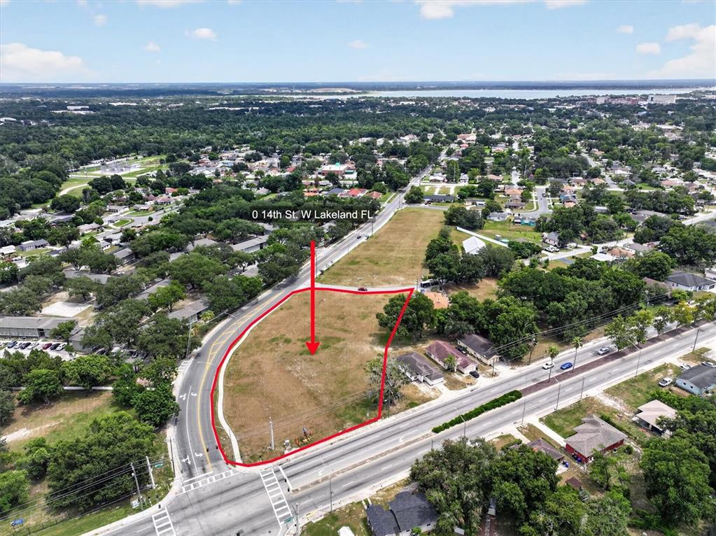 An aerial view shows a vacant, grass-covered corner lot outlined in red next to a road — 14TH STREET W, LAKELAND, FL