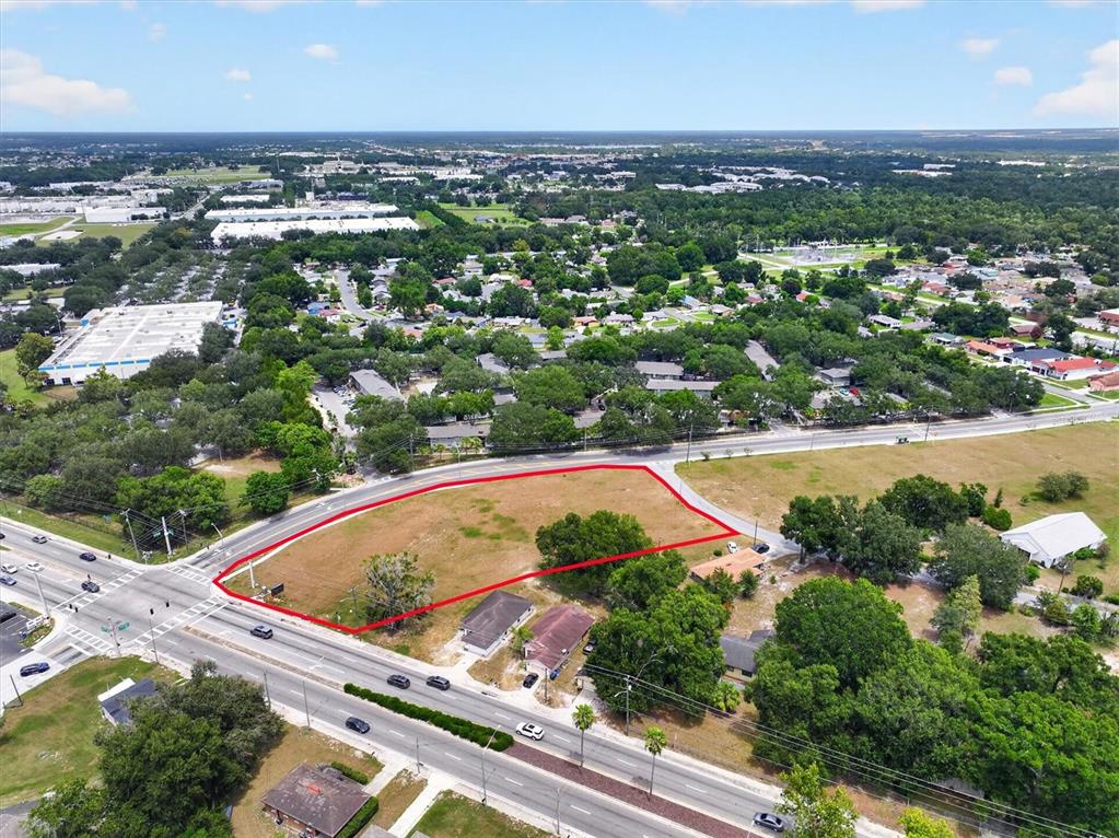 An aerial view shows a vacant, grass-covered corner lot outlined in red near a road — 14TH STREET W, LAKELAND, FL