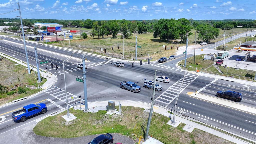 An aerial view shows a paved intersection with traffic lights, vehicles, and surrounding grassy lots — 75 SAGE ROAD, WINTER HAVEN, FL