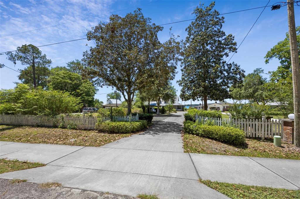 A concrete driveway leads toward a house framed by two large trees and white fencing — 7430 SW COUNTY ROAD 18, HAMPTON, FL