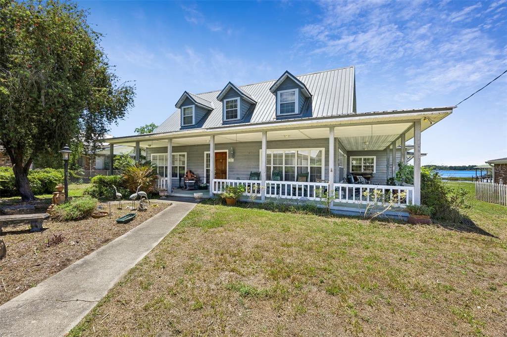 A gray house with a metal roof, dormer windows, and a large front porch faces water — 7430 SW COUNTY ROAD 18, HAMPTON, FL