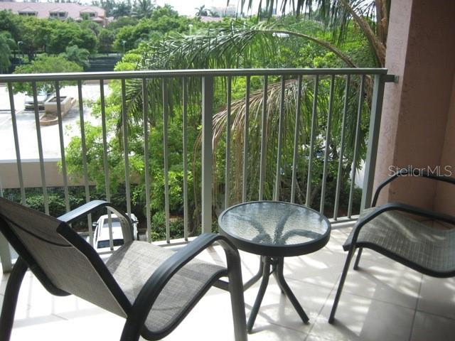 A balcony features two chairs and a small glass table overlooking trees and a parking lot — 19655 E COUNTRY CLUB DRIVE UNIT 6403, AVENTURA, FL