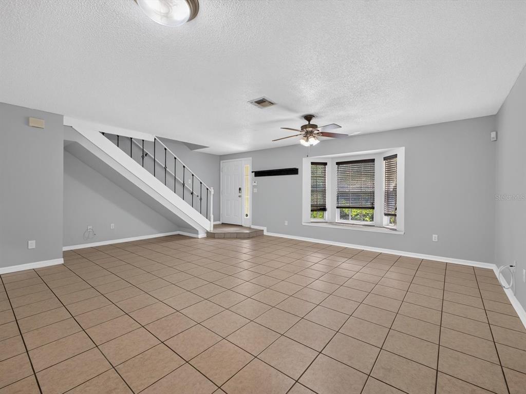 A living room with light gray walls, tile flooring, a staircase, and a bay window — 958 SYKES COURT UNIT 104, ORLANDO, FL