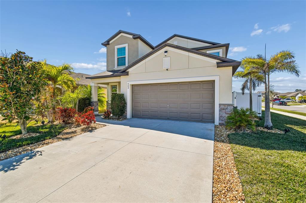 A two-story suburban house features a tan stucco exterior, a two-car garage, and landscaping — 984 OLIVE CONCH STREET, RUSKIN, FL