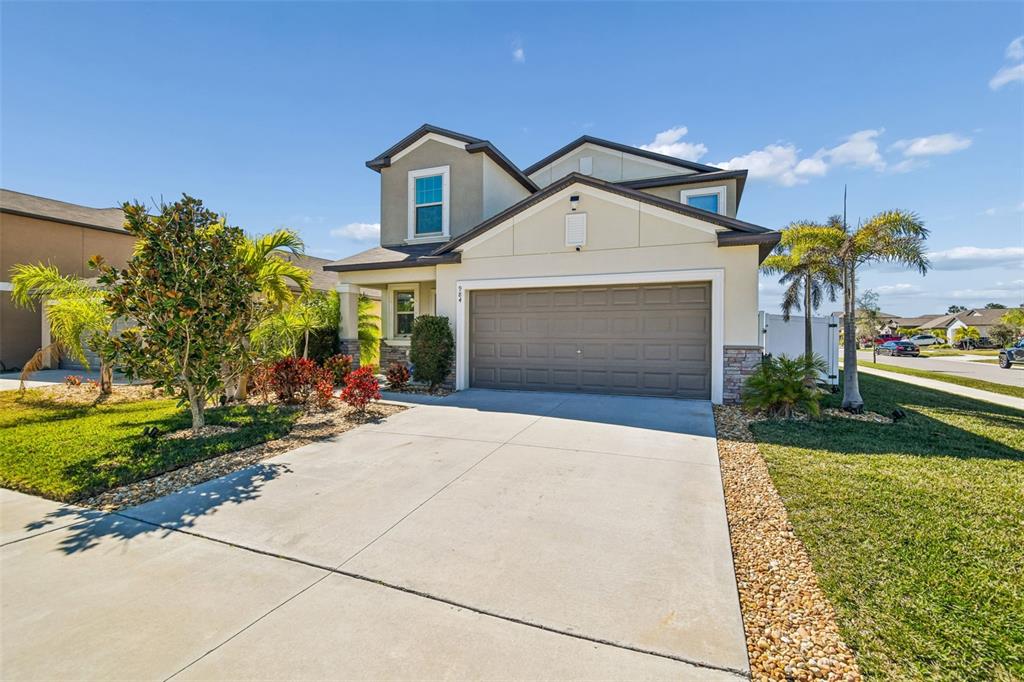 A two-story suburban house features a beige stucco exterior, stone accents, and a two-car garage — 984 OLIVE CONCH STREET, RUSKIN, FL
