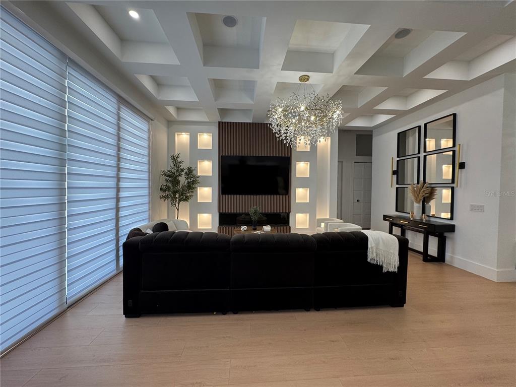 A living room features a coffered ceiling, a slatted wood accent wall, and a crystal chandelier — 8143 WHEYSTONE DRIVE, WEBSTER, FL