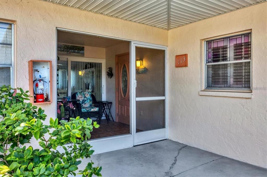 A covered front porch features a screen door, a fire extinguisher, and a front door — 460 BASE AVENUE E UNIT 113, VENICE, FL