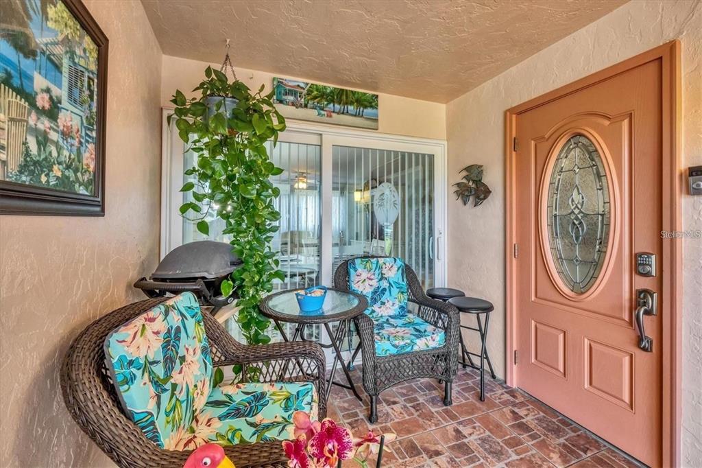 A covered patio features wicker furniture, a small glass table, and a salmon-colored front door — 460 BASE AVENUE E UNIT 113, VENICE, FL