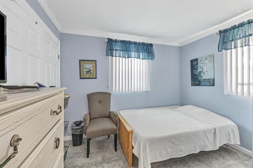 A bedroom with light blue walls, tile flooring, a bed, and a striped armchair — 460 BASE AVENUE E UNIT 113, VENICE, FL