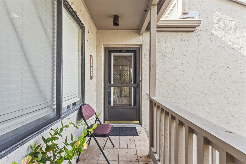 A covered entryway features a tiled floor, a brown storm door, and a folding chair — 1633 BOATHOUSE CIRCLE UNIT 232, SARASOTA, FL