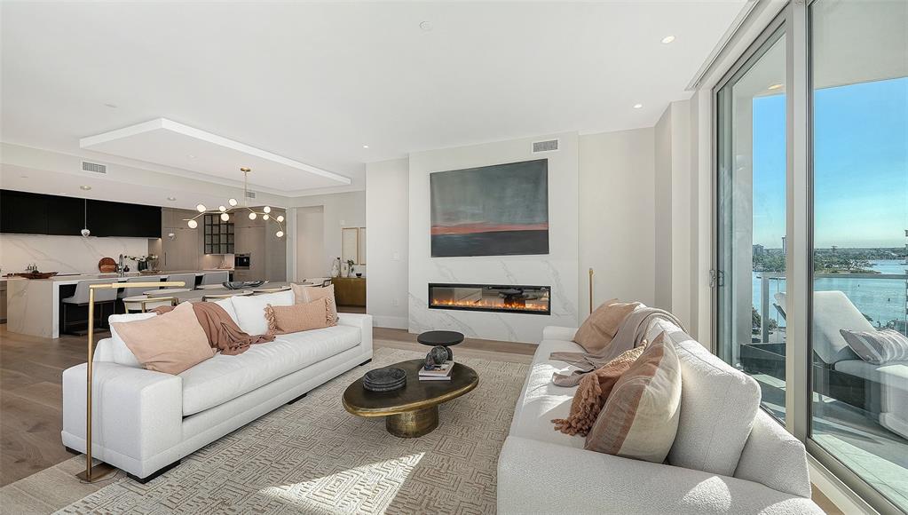 A bright living room features white sofas, modern coffee tables, and floor-to-ceiling windows overlooking water — 253 GOLDEN GATE POINT UNIT 701, SARASOTA, FL