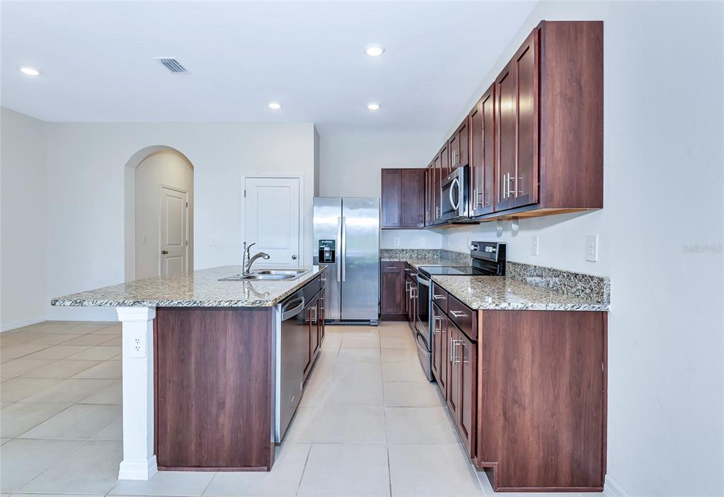 A kitchen features dark wood cabinets, granite countertops, stainless steel appliances, and a central island — 8657 MILESTONE DRIVE, SARASOTA, FL