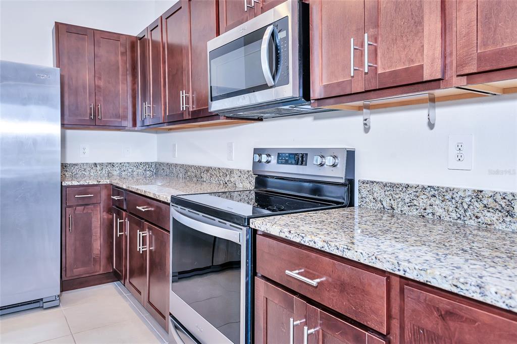 A kitchen features dark wood cabinets, granite countertops, and stainless steel appliances — 8657 MILESTONE DRIVE, SARASOTA, FL