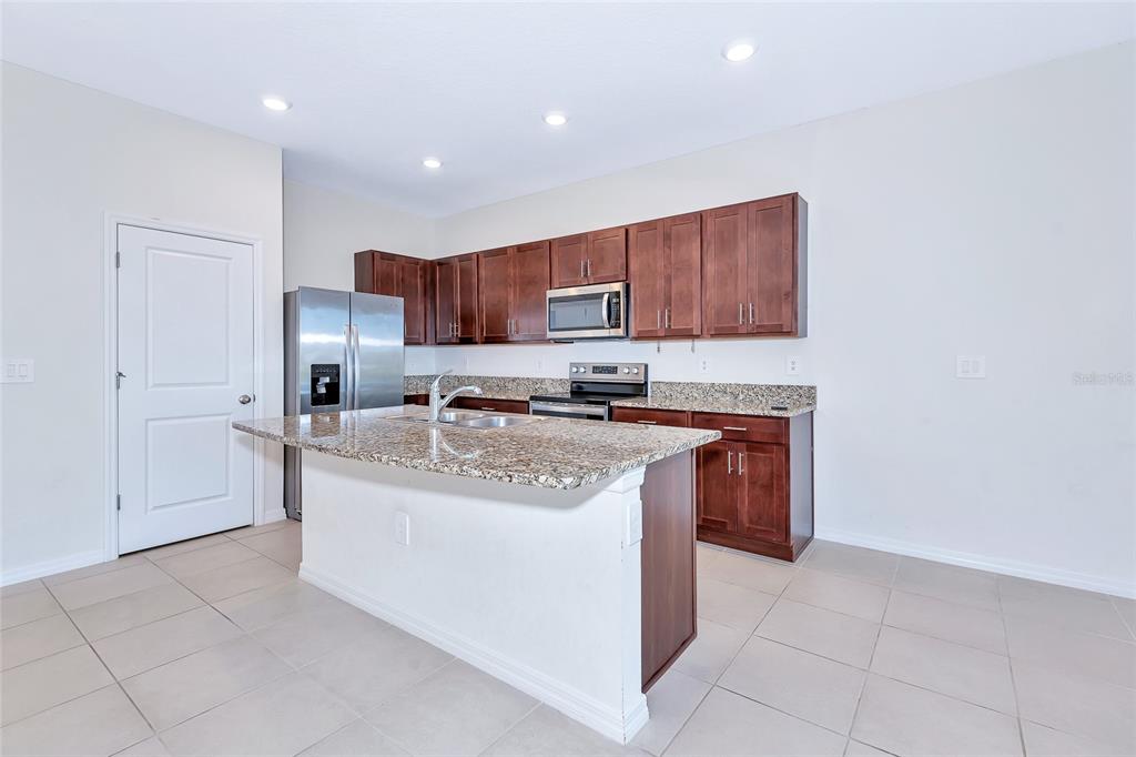 A kitchen features dark wood cabinets, granite countertops, a center island, and stainless steel appliances — 8657 MILESTONE DRIVE, SARASOTA, FL