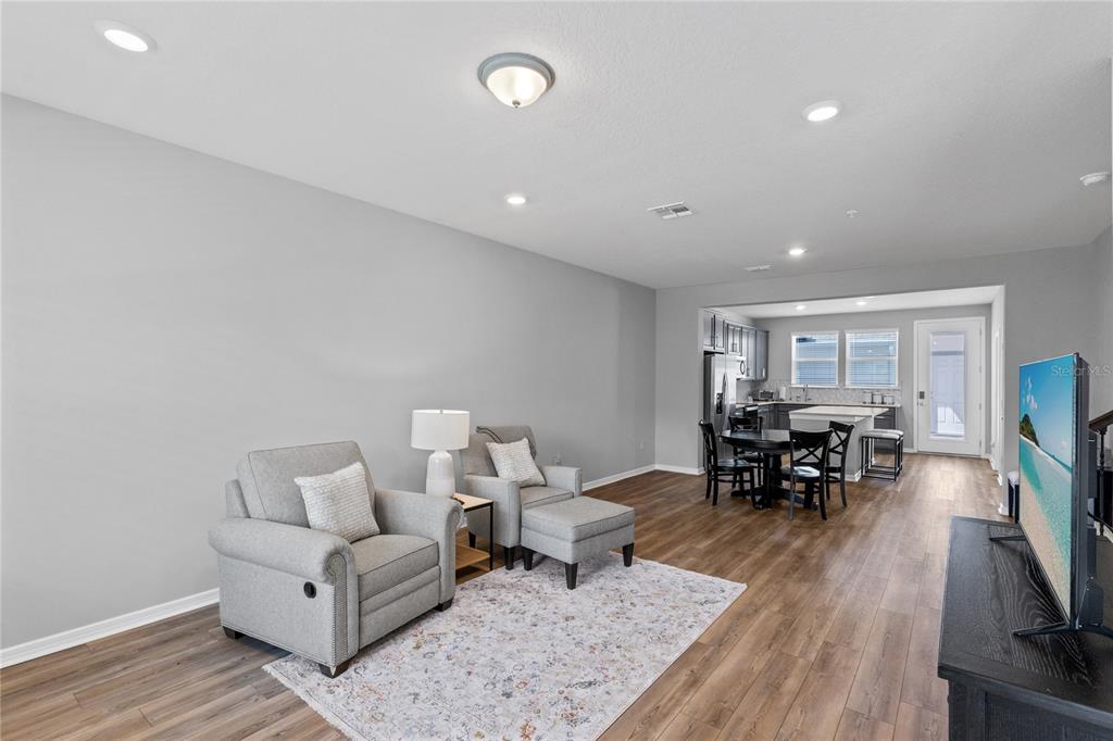 A living room with gray walls and wood-look flooring opens into a kitchen with dining area — 14376 SAPELO BEACH DRIVE, ORLANDO, FL