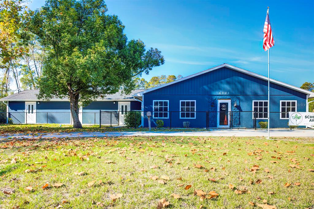A blue, single-story building with a flag pole stands behind a lawn covered in leaves — 6001 DELTONA BOULEVARD, SPRING HILL, FL