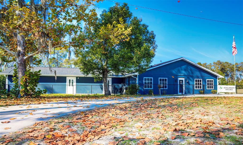 A blue single-story building sits behind a chain-link fence with a large tree in front — 6001 DELTONA BOULEVARD, SPRING HILL, FL