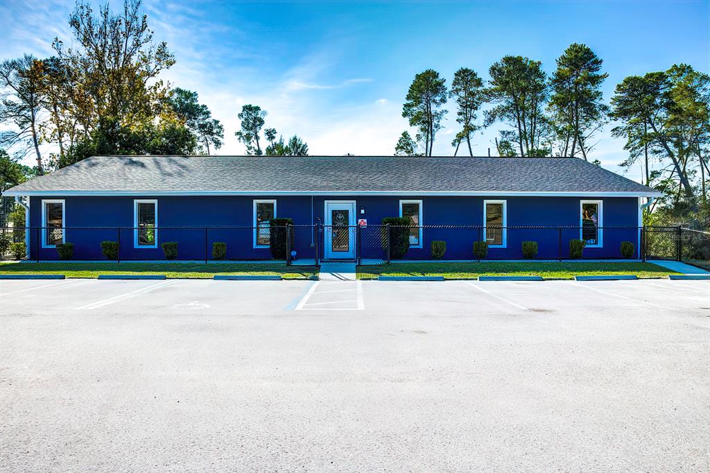 A single-story blue building with a gray roof sits behind a black chain-link fence — 6001 DELTONA BOULEVARD, SPRING HILL, FL