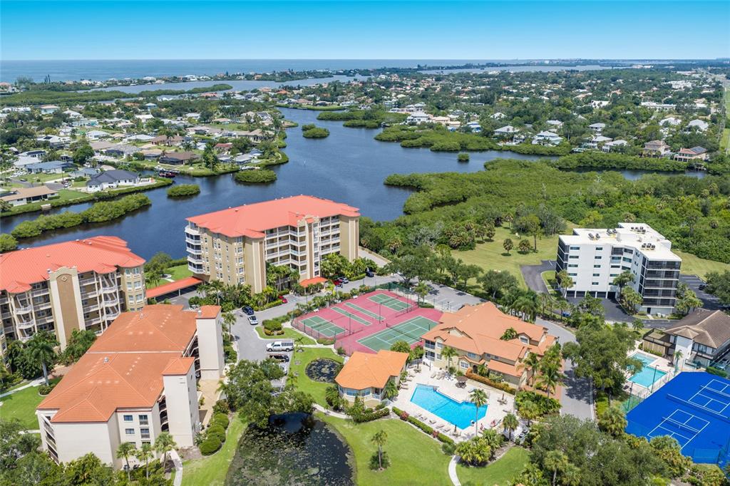 An aerial view of a residential complex featuring multi-story buildings, tennis courts, and a pool — 5100 JESSIE HARBOR DRIVE UNIT 404, OSPREY, FL
