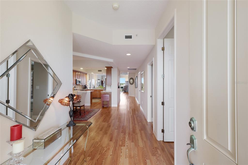 A hallway with hardwood floors leads from an entryway toward an open-concept kitchen and living area — 5100 JESSIE HARBOR DRIVE UNIT 404, OSPREY, FL