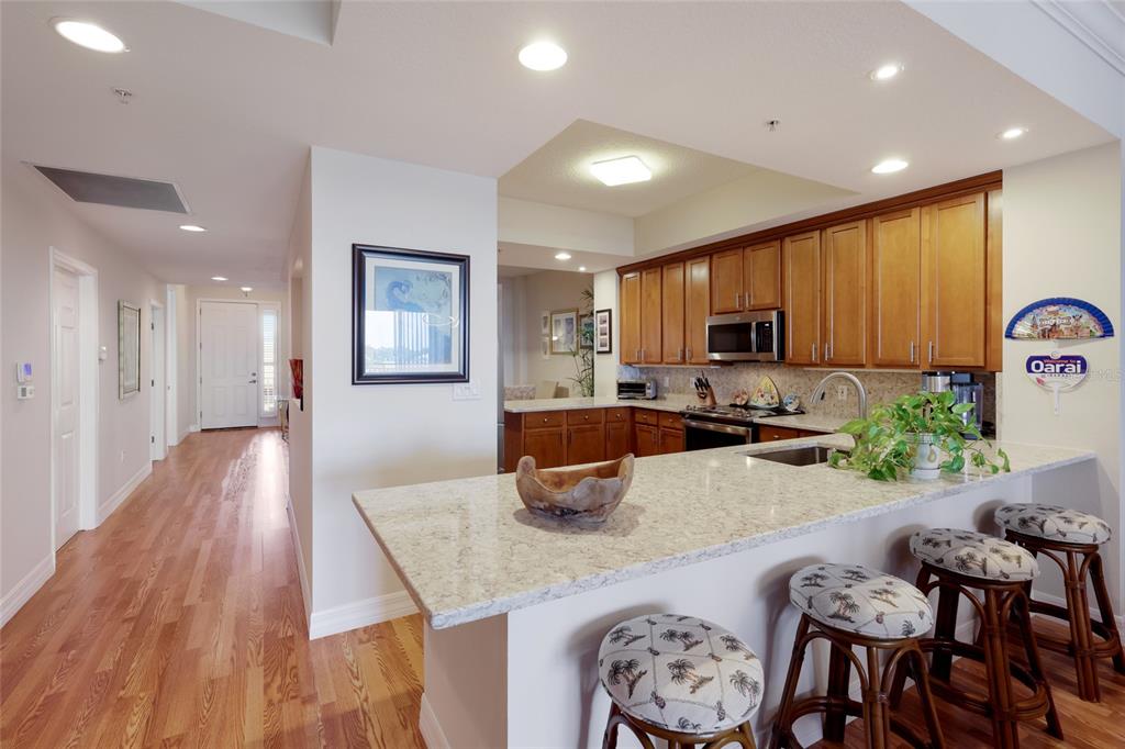 A kitchen with wood cabinets, granite countertops, and a breakfast bar with three stools — 5100 JESSIE HARBOR DRIVE UNIT 404, OSPREY, FL