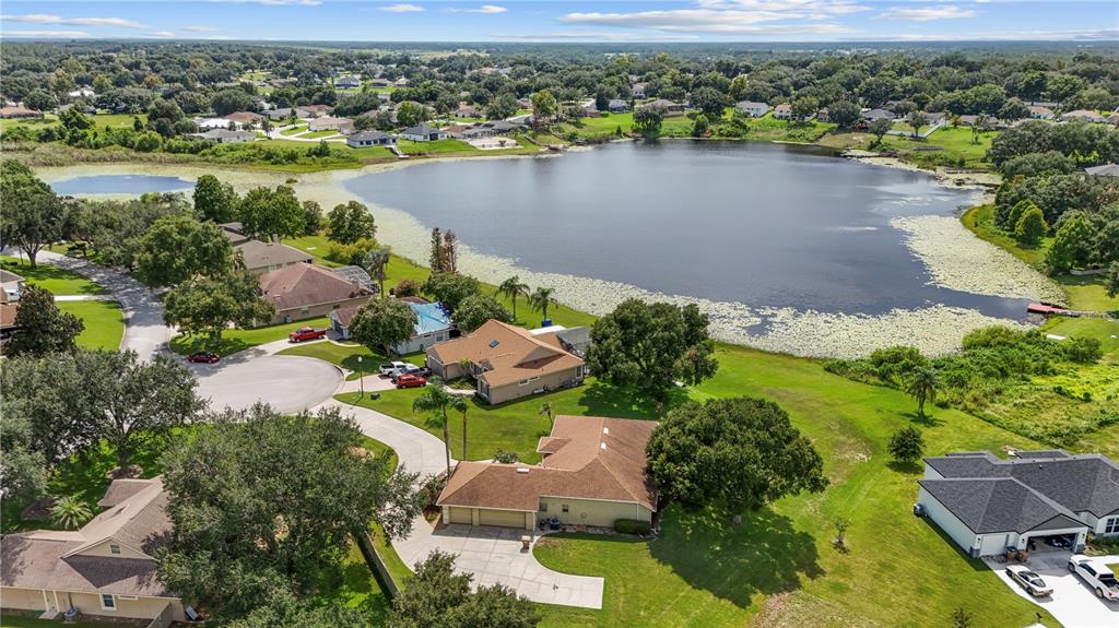 An aerial view shows suburban houses surrounding a large lake with lily pads — 11546 NICE COURT, CLERMONT, FL