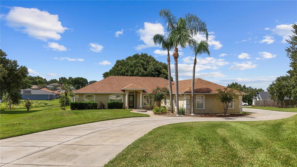 A single-story house with a tan exterior, brown roof, and palm trees in the front yard — 11546 NICE COURT, CLERMONT, FL