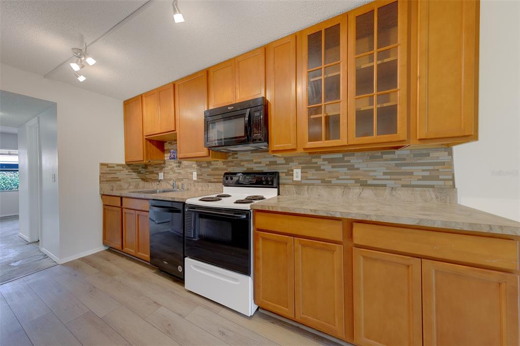 A kitchen features wood cabinets, a black microwave and dishwasher, and a tiled backsplash — 5090 BAY STREET NE UNIT 124, ST PETERSBURG, FL