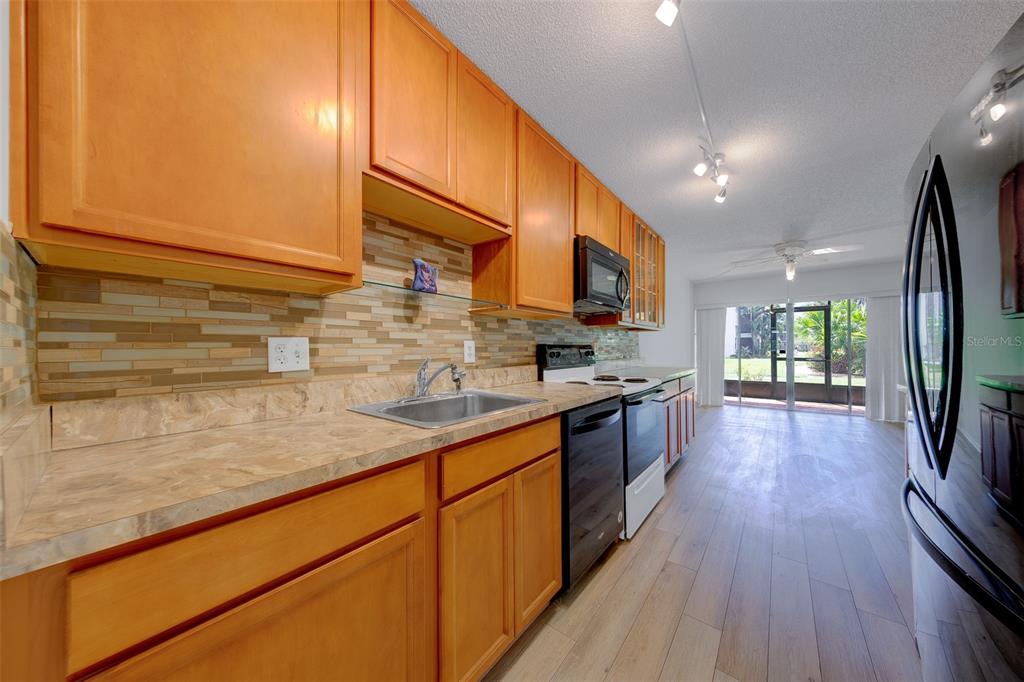 A galley kitchen features light wood cabinets, laminate countertops, and a view of the patio — 5090 BAY STREET NE UNIT 124, ST PETERSBURG, FL