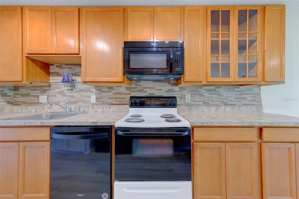 A kitchen features wood cabinets, a black microwave and stove, and a tiled backsplash — 5090 BAY STREET NE UNIT 124, ST PETERSBURG, FL