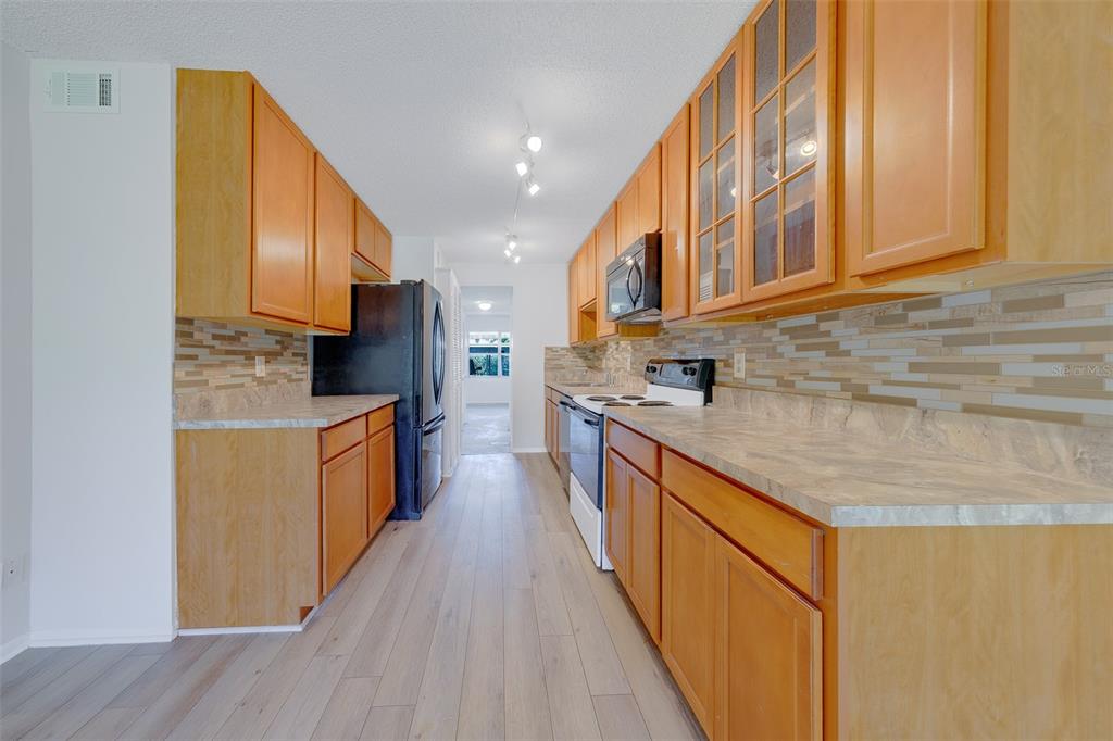 A galley kitchen features wood cabinets, light countertops, a tiled backsplash, and stainless steel appliances — 5090 BAY STREET NE UNIT 124, ST PETERSBURG, FL