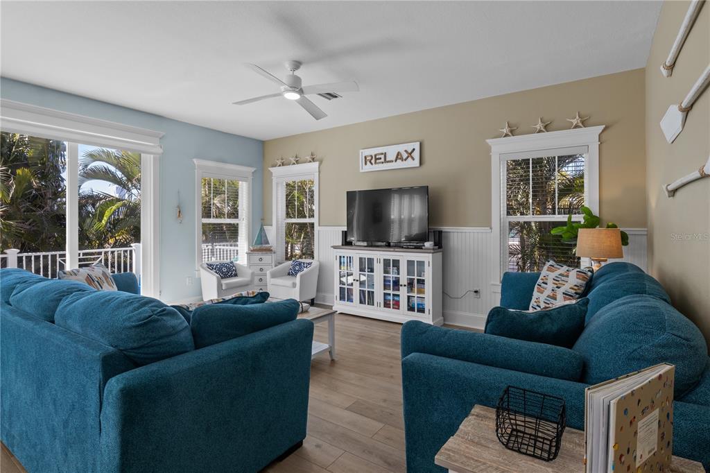 A living room features blue sofas, a television on a white console, and coastal decor — 6908 HOLMES BOULEVARD, HOLMES BEACH, FL