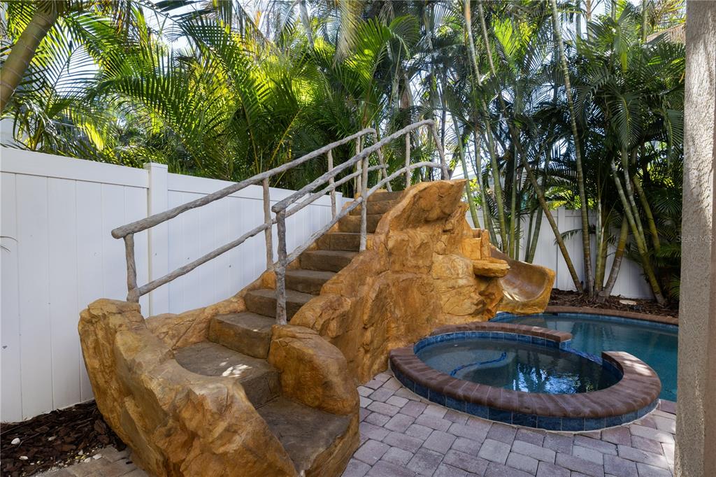 A backyard pool area features a faux-rock staircase with a slide and a small hot tub — 6908 HOLMES BOULEVARD, HOLMES BEACH, FL