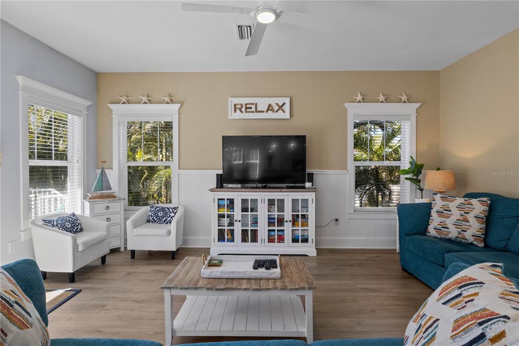 A coastal-themed living room features a television, white media console, and blue sofas — 6908 HOLMES BOULEVARD, HOLMES BEACH, FL