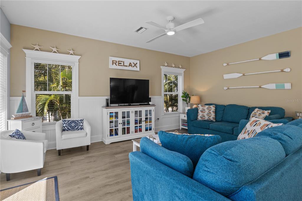 A living room features blue sofas, white armchairs, a television, and nautical wall decor — 6908 HOLMES BOULEVARD, HOLMES BEACH, FL